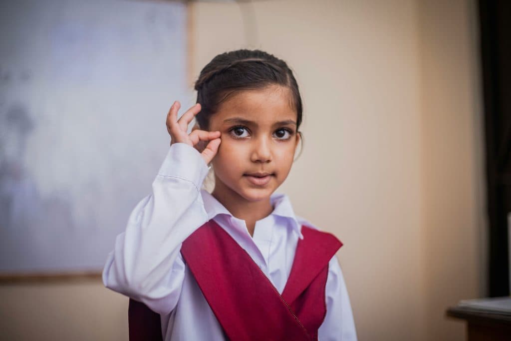 Une petite fille met sa main qui forme une pince proche de ses yeux, représentant l'utilisation de gestes et signes pour échanger
