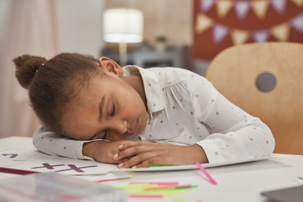 Image d’un enfant fatigué, qui se frotte les yeux en faisant ses devoirs