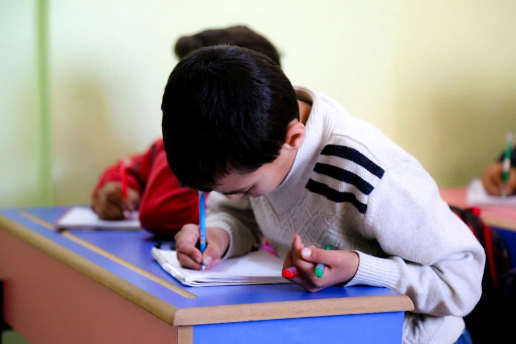 Un petit garçon se concentre sur son cahier en classe. Il est en plein apprentissage de l'écriture manuscrite.