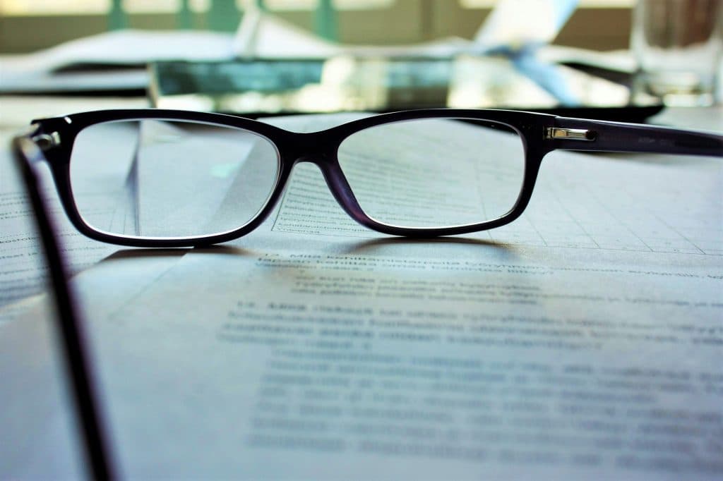 Des lunettes sont posées sur une feuille avec du texte. Ceci représente la nécessité de faire une évaluation des progrès d'une personne autiste lors de son accompagnement..